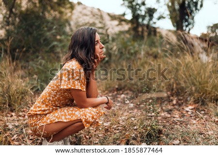 Thoughtful beautiful brunette woman wearing a dress squatting in the woods
