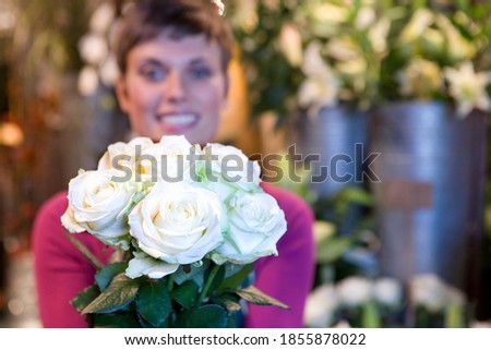 Young female florist holding a bouquet of flowers in her hand and smiling at the camera