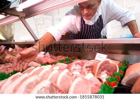 Middle-aged butcher reaching out for pork chops kept in the refrigerator in his meat shop