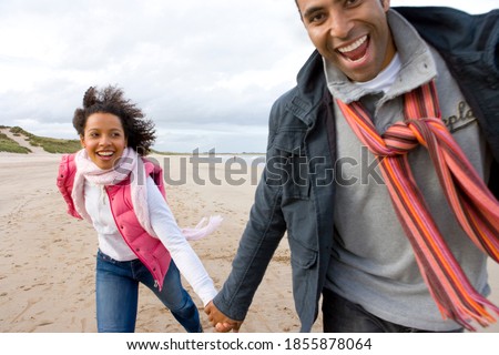 Close up of a young couple running on the beach while holding hands on an overcast, windy day Royalty-Free Stock Photo #1855878064