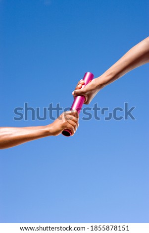 Close up of a female athlete passing a relay baton to her teammate on a bright, sunny day at an athletics competition Royalty-Free Stock Photo #1855878151