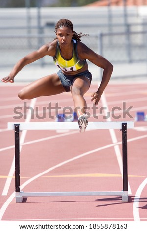 Young African female runner jumping over a hurdle at an athletics event out at the track on a bright, sunny day Royalty-Free Stock Photo #1855878163