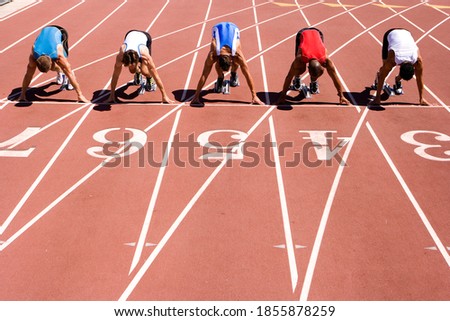 Male sprinters waiting for the start of a sprint race on their starting blocks behind lane markings at an athletics event on the track Royalty-Free Stock Photo #1855878259
