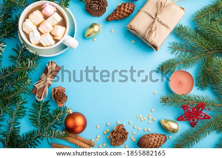 Christmas or New Year frame composition. Decorations, box, cinnamon, cones, fir and spruce branches, cup of coffee, on a blue paper background. Top view, copy space, flat lay.