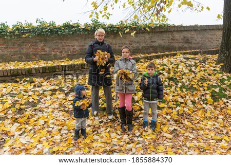 A mother with three children is playing with autumn leaves. Family Playing With Autumn Leaves In Garden 