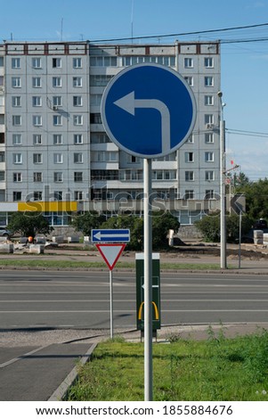 Traffic sign instructing to turn left. Blue round sign on a pillar with a white arrow. Regulation of vehicle traffic.