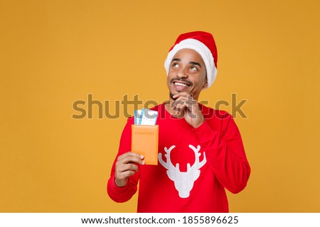 African traveler tourist Santa man in Christmas hat hold passport tickets put hand prop up on chin dream isolated on yellow background Happy New Year celebration holiday concept Tattoo translate life
