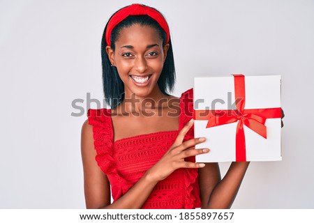 Young african american woman holding gift looking positive and happy standing and smiling with a confident smile showing teeth 