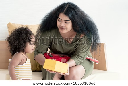 African black mother giving a gift box to her little daughter for celebrate birthday at home in living room. Family Concept.