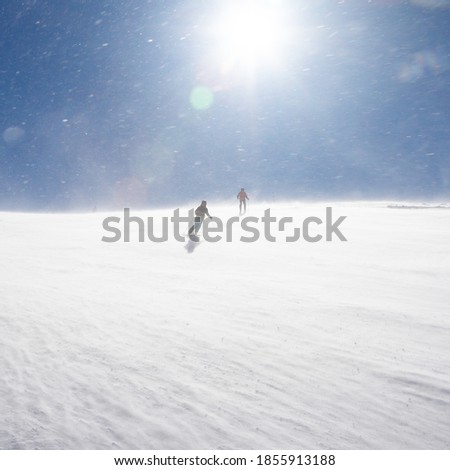 Snowstorm on a sunny day. Skiers go down the slope. Bad Gastein, Austrian Alps.
