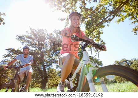 Close up of a happy couple riding mountain bikes in a rural field Royalty-Free Stock Photo #1855918192