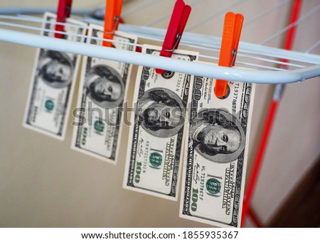 four hundred-dollar bills hang suspended from red and orange clothespins on a white and red metal dryer in the room . money