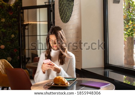 Woman holding smartphone, smiling, having breakfast in the restaurant