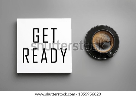 Card with text Get Ready and cup of coffee on light grey table, flat lay