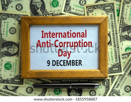 Wooden picture frame with inscription 'International Anti-Corruption Day 9 december' on beautiful background from dollar bills and metalic pen. Business concept.