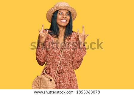 Young african american woman wearing summer hat shouting with crazy expression doing rock symbol with hands up. music star. heavy concept. 