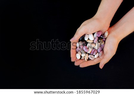 Beans. Handful of multicolored beans in female hands on a black background Royalty-Free Stock Photo #1855967029