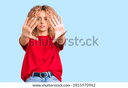 Young blonde woman with curly hair wearing casual red tshirt doing frame using hands palms and fingers, camera perspective 
