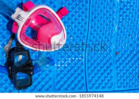 A full-face and traditional black mask for snorkeling and diving lies on the blue cover. Place for text. Pink for children and girls. Sea vacation concept. Copy space