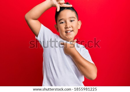 Little boy hispanic kid wearing casual white tshirt smiling making frame with hands and fingers with happy face. creativity and photography concept. 