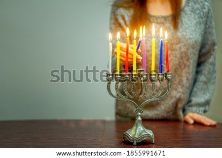 Jewish Woman Celebrating Holidays Hanukkah Alone DuringThe COVID-19 Pandemic. Woman Lighting Hanukkah Candles In A Menorah.