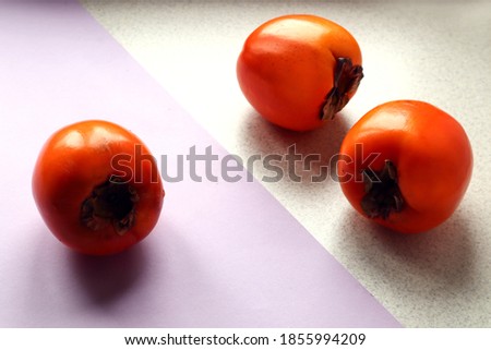 Three ripe persimmon fruits on a pastel and gray background, close-up, side view, space for text