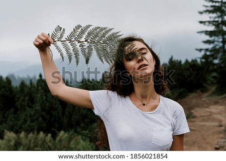 Girl is holding leaf of fern and travelling in the mountains. Foggy day. Hiking and climbing up to the peak of the mountain. Beautiful nature of Ukraine.