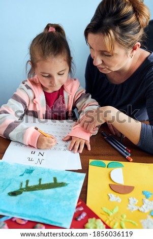 Little girl preschooler learning to write letters with help of her mother. Kid writing letters, drawing pictures, making stuff with paper, doing a homework. Concept of early education