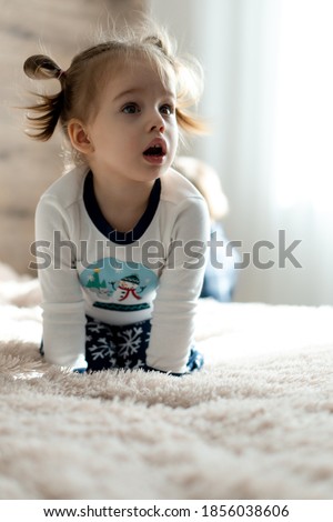 childhood, technology, infant, minor concepts - one cute child baby girl watch cartoon on phone, smartphone on soft white bed in sunny room. kid in pajamas speak by video conference on gadget indoors
