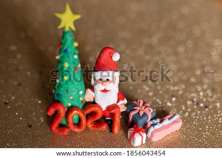 Playful clay christmas concept. Colorful handmade miniature Christmas tree, presents and Santa Claus in gold background. 2021 new year.