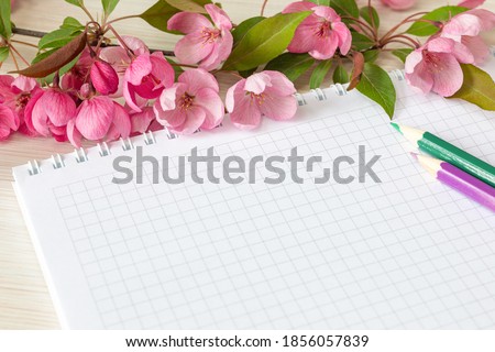 Empty notebook and pink apple blossoms on the white table. Woman working desk.