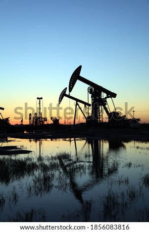 Oil field site, in the evening, oil pumps are running, Silhouette of beam pumping unit