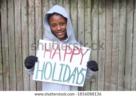 Kid holding red and green happy holiday sign standing outdoors fence background
