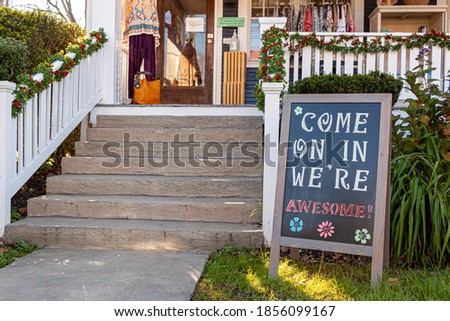 A sandwich board with a welcoming notice on it which reads : " Come on in, we are awesome " is placed in the front yard of a small local clothing shop in historic Clifton, Virginia.