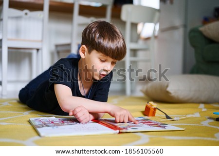 Preschool caucasian boy lying on the floor at home, reading books and watching pictures. Home education concept