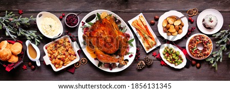 Traditional Christmas turkey dinner. Top view panoramic table scene on a dark wood banner background. Turkey, potatoes and sides, stuffing, fruit cake and plum pudding. Royalty-Free Stock Photo #1856131345