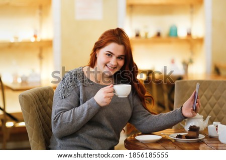 Caucasian beautiful plus size lady overweight woman drinks coffee and works. Difficult choice concept, diet or delicacy. Brunette woman with long hair in a cafe
