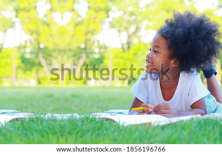 Girl lying on the lawn reading a book in the park  concept of children learning