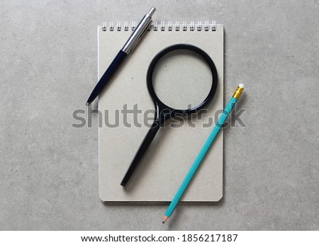 A spring notebook with a sheet of craft paper A5 with black magnifying glass, a ballpoint pen and simple green graphite pencil on light grey concrete background. Concept of new idea, business plan and