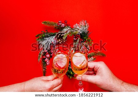 Top view Two male and female hands holds glasses of champagne, flat lay wreath on a red background