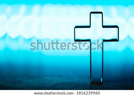 Christian cross on blue background with soft bokeh lights background. Copy space. Banner. Church worship, salvation concept. Faith symbol in Jesus Christ. Holy cross for good friday, Easter day.