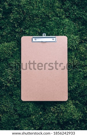 Top view of clipboard, paper, pen on green grass, moss background. Copy space. Flat lay. Office mock up, remote job. Wild nature, ecology concept. Sustainable, organic, zero waste lifestyle.