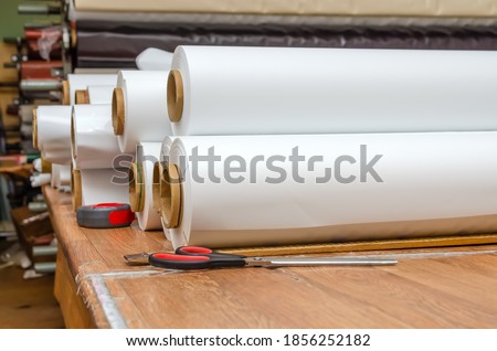 White rolls of PVC film are on the table in the workshop for the production of stretch ceilings. Production of stretch ceilings. Royalty-Free Stock Photo #1856252182