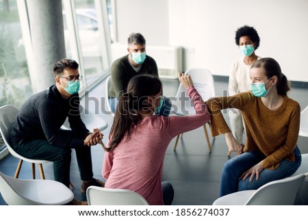Group therapy participants elbow bumping and wearing face masks due to coronavirus pandemic.  Royalty-Free Stock Photo #1856274037