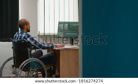 Freelancer photo designer with disability in wheelchair editing post production a video project creating content in modern company office. Videographer working from photo studio.