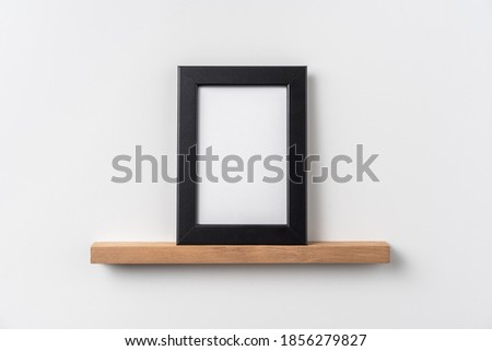 Design concept - front view of vertical black wood photo frame on bookshelf and white wall for mockup