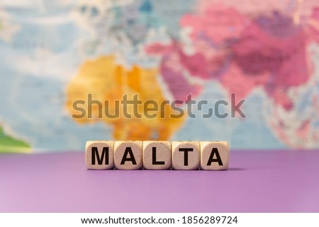 The word Malta written with wooden dices in front of a purple background and a geographic map