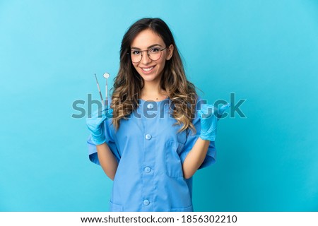 Woman dentist holding tools over isolated on blue background pointing to the side to present a product Royalty-Free Stock Photo #1856302210