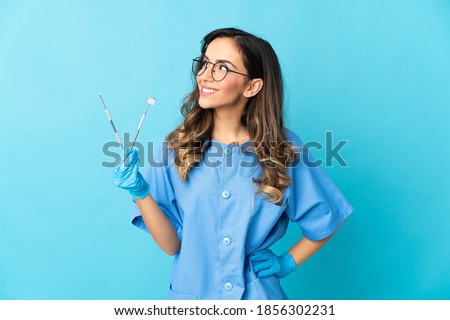 Woman dentist holding tools over isolated on blue background thinking an idea while looking up Royalty-Free Stock Photo #1856302231