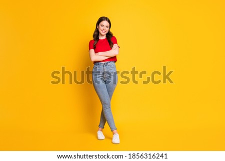 Full size photo of charming lady hold arms crossed wear casual red t-shirt cropped top jeans shoes isolated yellow color background